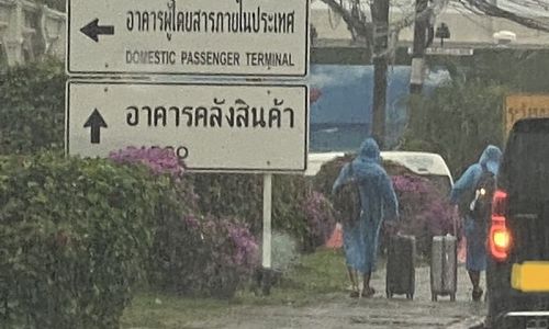 นักท่องเที่ยวลากกระเป๋าเดินทางตากฝน เพื่อมาขึ้นรถรับจ้างผ่านระบบอิเล็กทรอนิกส์ภายนอกบริเวณสนามบิน ภาพ: เฟซบุ๊ก ศูนย์ข้อมูลภูเก็ต